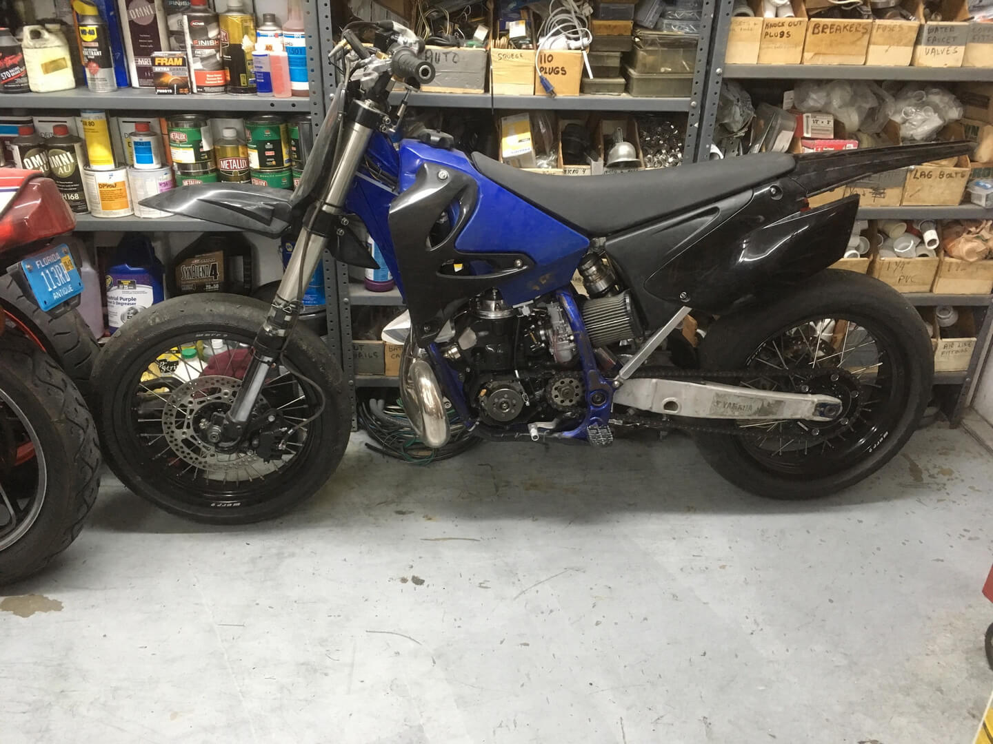 A blue motorcycle parked in a garage next to shelves.