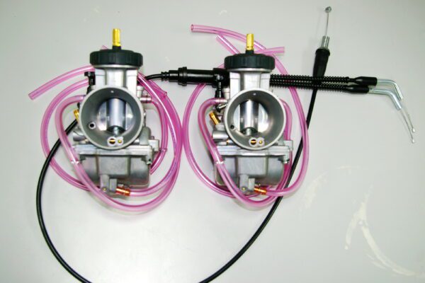 Two 38mm Keihin "PWK" Air Striker Carburetor Kits, Part 22-5767, with pink hoses attached to them.