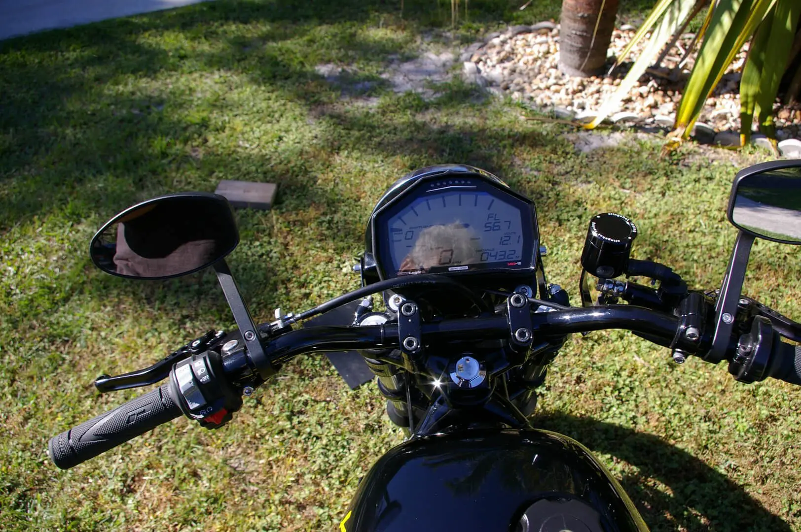 A motorcycle is parked in the grass near some bushes.