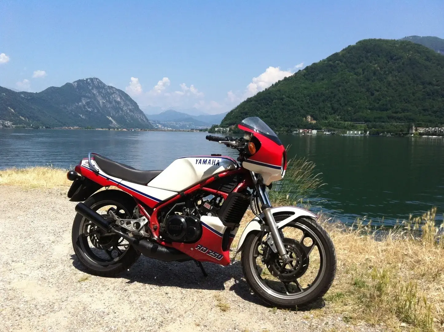 A red and white motorcycle parked on the side of a lake.