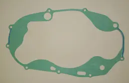 A single RZ 350/Banshee Clutch Cover Gasket rests against a white wall.