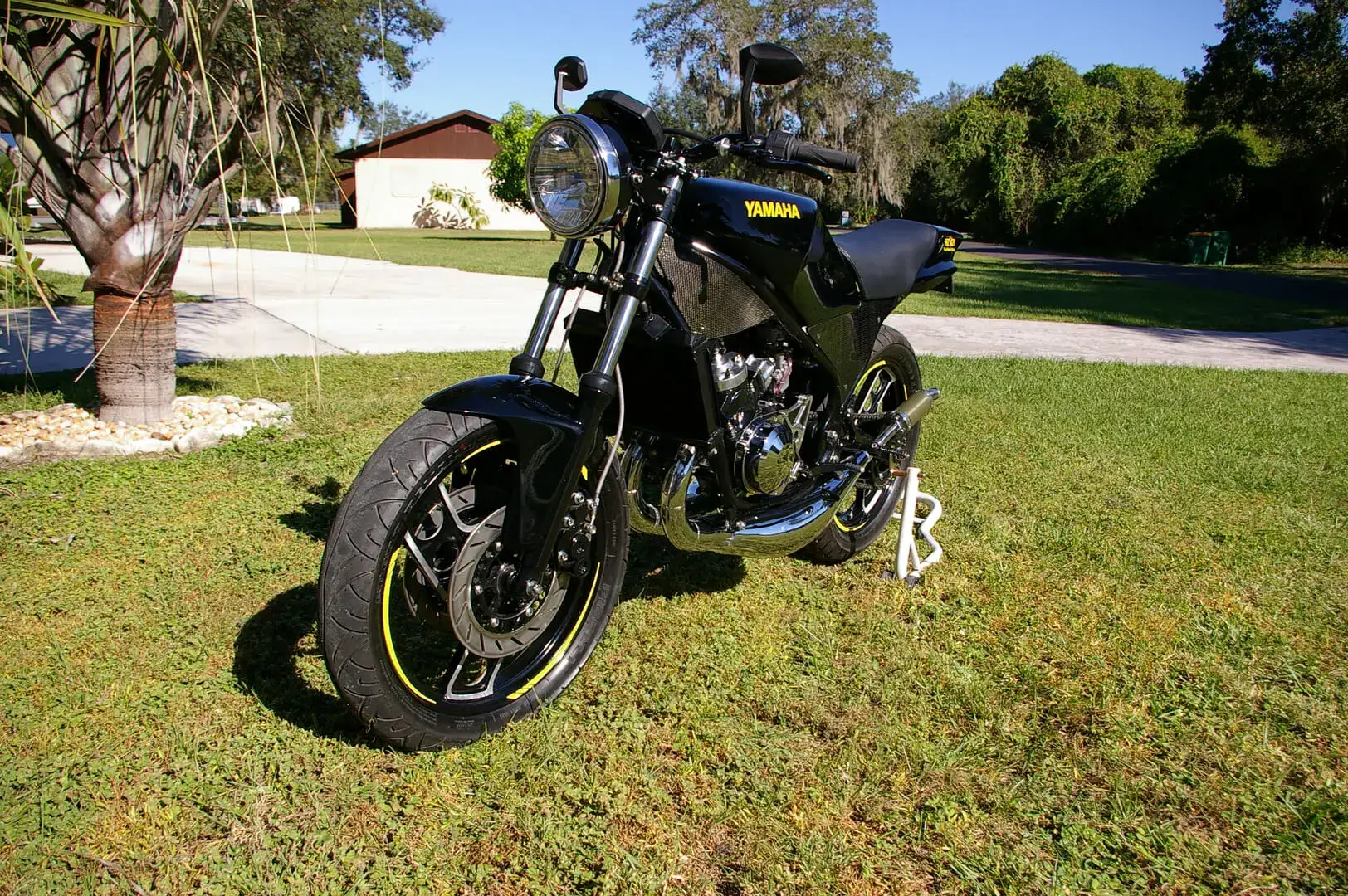 A black motorcycle parked in the grass near some trees.